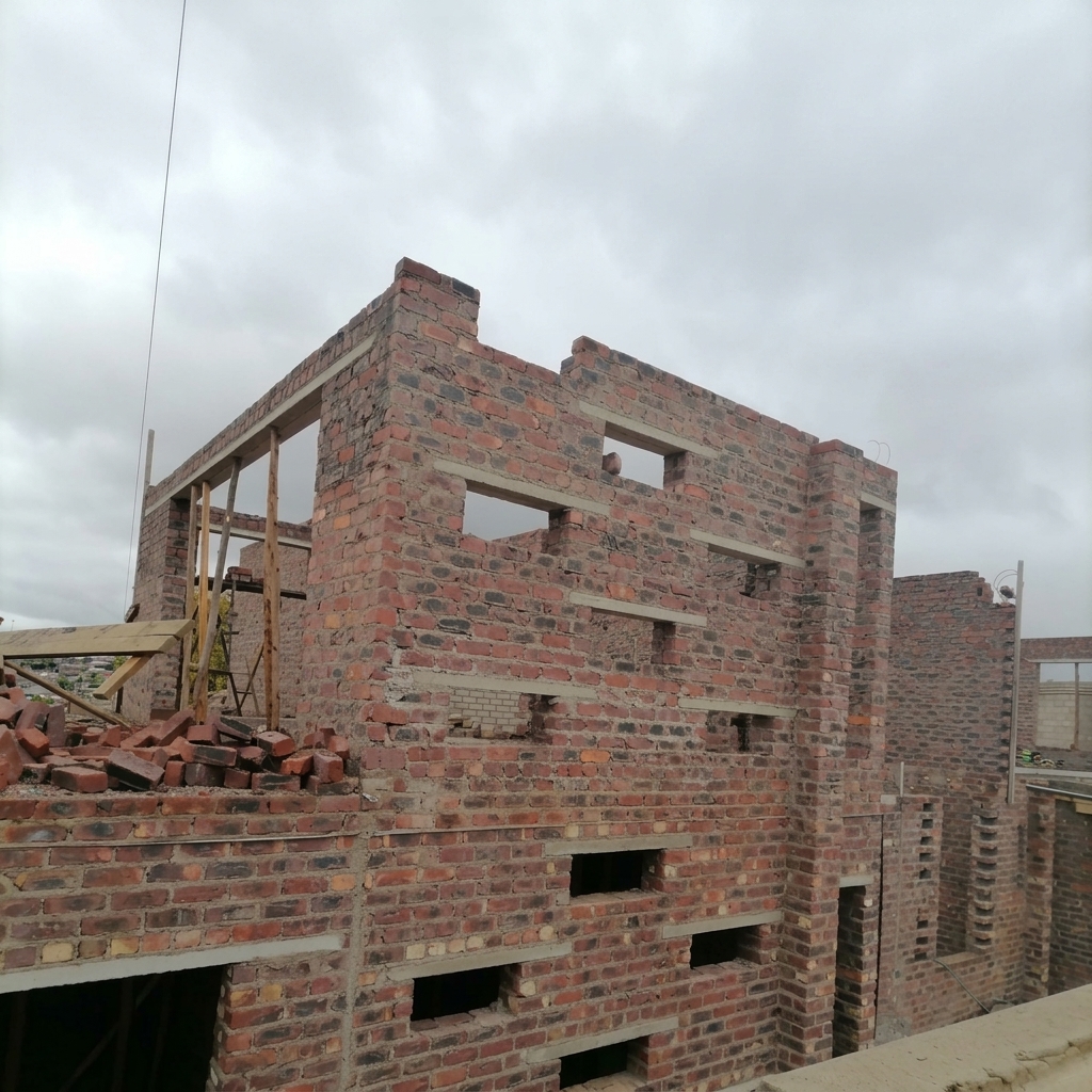 Branded Mbozisi photo of a brick shell building under construction with concrete lintels in place.